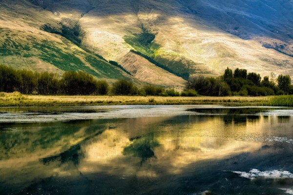 By Michael Piraino New Zealand South Island foothills reflected in river and pond at sunrise