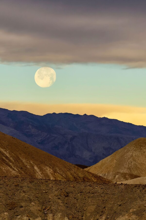 By Michael Piraino Full moon setting over colorful hills in Death Valley