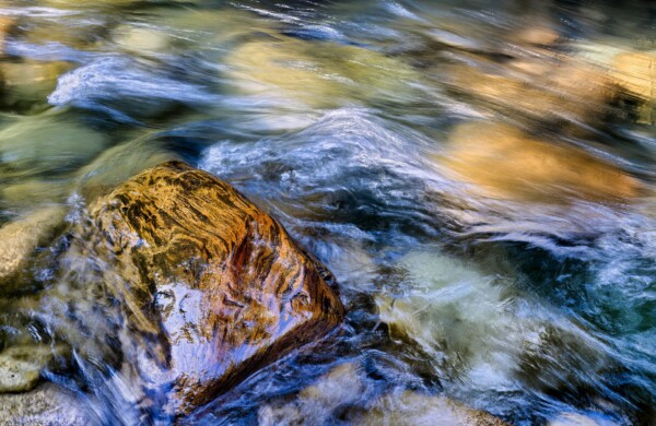 By Michael Piraino Flowing river vibrant red and yellow with boulder